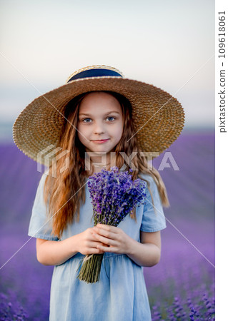 Lavender sunset girl. A laughing girl in a blue dress with flowing hair in a hat walks through a lilac field, holds a bouquet of lavender in her hands. Lavender sunset girl. A laughing girl in a blue dress with flowing hair in a hat walks through a lilac field, holds a bouquet of lavender in her hands. 109618061