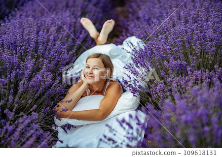 A middle-aged woman lies in a lavender field and enjoys aromatherapy. Aromatherapy concept, lavender oil, photo session in lavender 109618131
