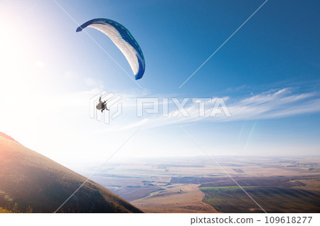 paraglider flies in the blue sky against a background of clouds and blue sky. Paragliding in the sky on a sunny day paraglider flies in the blue sky against a background of clouds and blue sky. Paragliding in the sky on a sunny day 109618277