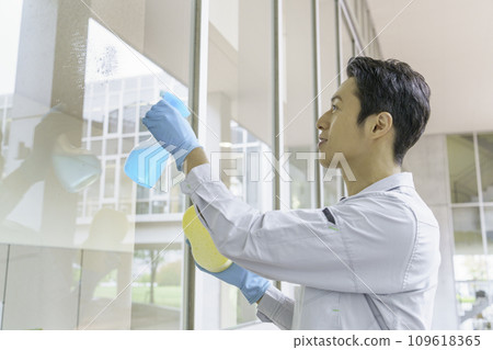 A male cleaner cleaning windows in an office. Photography cooperation: Ariake College of Education and Arts A male cleaner cleaning windows in an office. Photography cooperation: Ariake College of Education and Arts 109618365