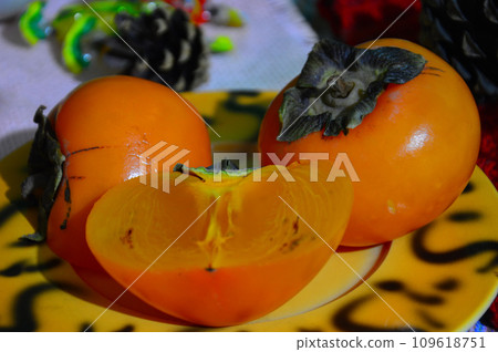 Ripe persimmon fruits on a plate on the table. Persimmon is a very popular fruit. Ripe persimmon fruits on a plate on the table. Persimmon is a very popular fruit. 109618751