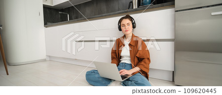 Remote workplace. Young woman works from home, sits on floor with headphones and laptop, student doing homework, studying online 109620445