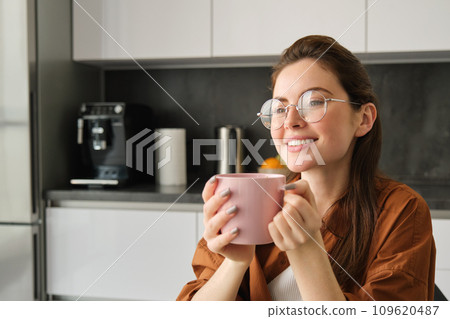 Beautiful young woman, drinking coffee, smiling and looking away with dreamy face, enjoying nice flavour and aroma 109620487