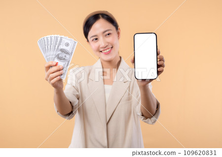 portrait of happy successful confident young asian business woman wearing white jacket holding smartphone and cash money dollar standing over beige background. millionaire business, shopping concept. 109620831
