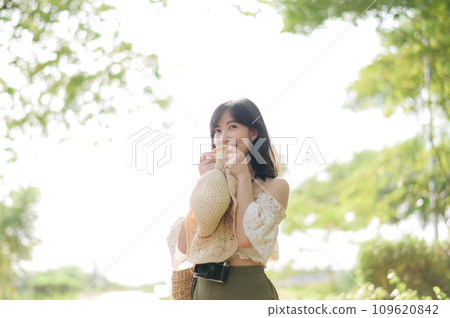 Portrait of asian young woman traveler with weaving hat and basket and a camera on green public park nature background. Journey trip lifestyle, world travel explorer or Asia summer tourism concept. Portrait of asian young woman traveler with weaving hat and basket and a camera on green public park nature background. Journey trip lifestyle, world travel explorer or Asia summer tourism concept. 109620842