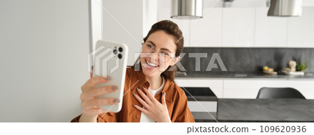 Beautiful young woman, social media blogger recording video, online video chatting on smartphone, standing at home with mobile phone 109620936