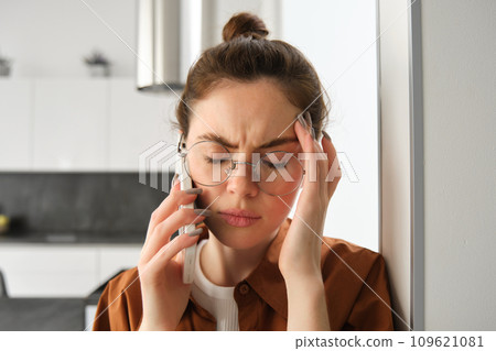 Close up portrait of young troubled, worried woman listens to voice message, having difficult phone conversation, answer a call and looking concerned, touching head 109621081