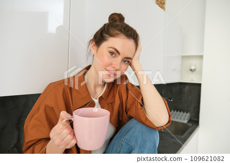 Portrait of young woman with cup of coffee, sits in kitchen and drinks aromatic drink at home, holds tea mug 109621082