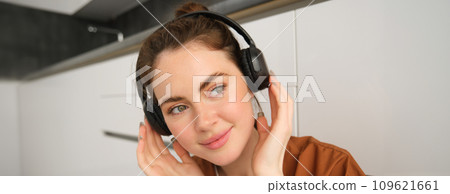 Close up shot of cute young woman in wireless headphones, listens to music and smiles, relaxes at home with favourite songs playing on her playlist 109621661