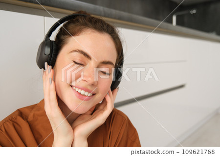 Close up portrait of beautiful brunette woman, listens to music in wireless headphones, has new earphones on her head, smiling and looking happy 109621768