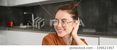 Close up portrait of brunette woman in glasses, beautiful female model sitting in kitchen, laughing and smiling, express carefree, positive emotion 109621907