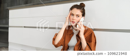 Portrait of woman calling her GP from home, holding smartphone, has headache or high fever 109621948