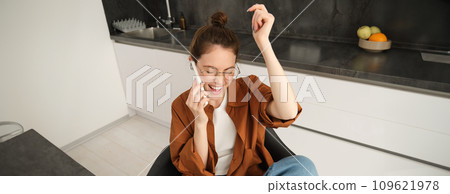 Portrait of woman receiving great news over the phone call, celebrates and jumps on chair from excitement during telephone conversation 109621978