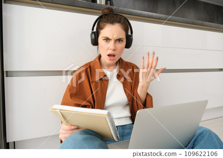 Confused and frustrated woman in headphones, student doesnt understand something while doing homework on laptop, looking annoyed at camera 109622106