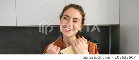 Portrait of young modern woman, 25 years old, standing in the kitchen with notebook, reading notes, student revising for exam 109622607