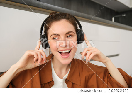 Carefree female model in wireless headphones, listens to music, enjoys favourite tunes in earphones, sings along and smiles Carefree female model in wireless headphones, listens to music, enjoys favourite tunes in earphones, sings along and smiles 109622923