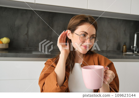 Portrait of lovely, tender young woman in glasses, sits at home with cup of tea. Girl in kitchen, enjoys drinking aromatic coffee 109623144
