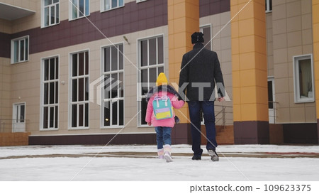 father takes child school holding his hand. happy family. snowy road school. father leads his little girl with school backpack through snow school. cold season. Dad holds hand child kid with backpack. father takes child school holding his hand. happy family. snowy road school. father leads his little girl with school backpack through snow school. cold season. Dad holds hand child kid with backpack. 109623375