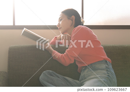 一位女士在客廳的沙發上放鬆地看書。 109623667