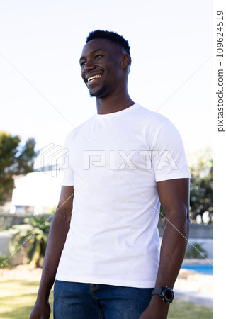Vertical image of smiling african american man in white t-shirt with copy space in garden 109624519