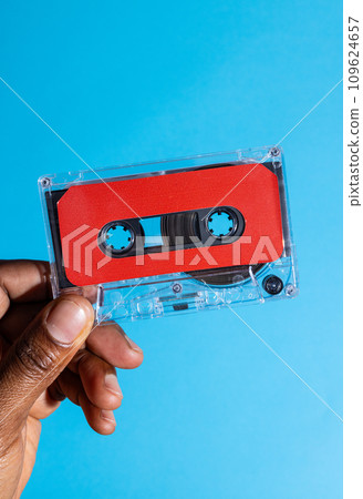 Close up of hand of african american man holding red cassette tape over blue background 109624657