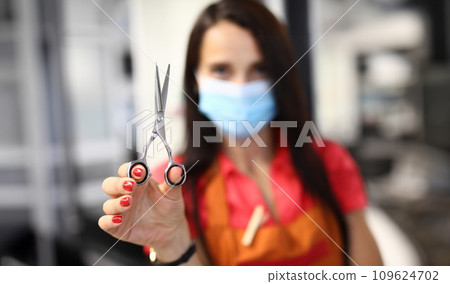 Woman hairdresser in protective mask holds scissors 109624702
