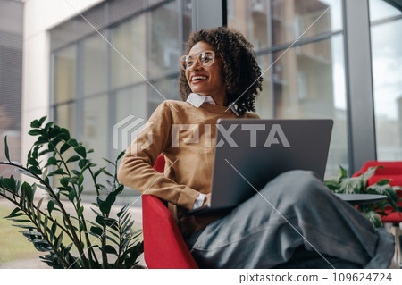 Smiling business woman using laptop while sitting on modern office background  109624724