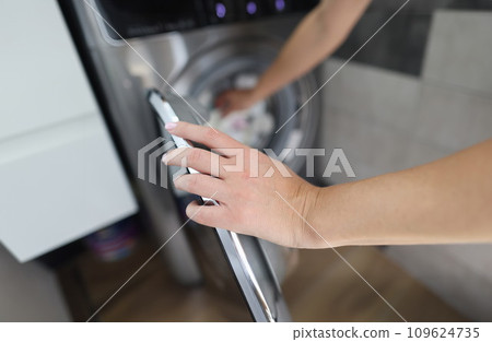 Woman hand fills drum of washing machine closeup Woman hand fills drum of washing machine closeup 109624735