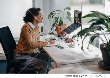 Smiling business woman have video conference with client and making notes sitting in office 109625110
