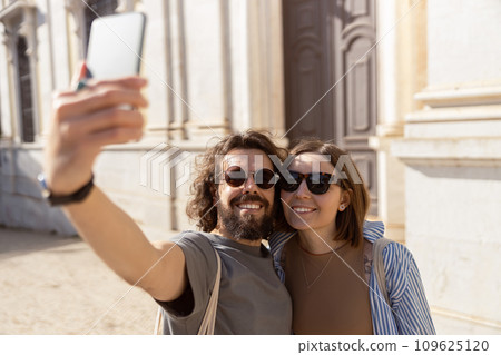 Smiling tourist couple walking in city street and making selfie on phone 109625120