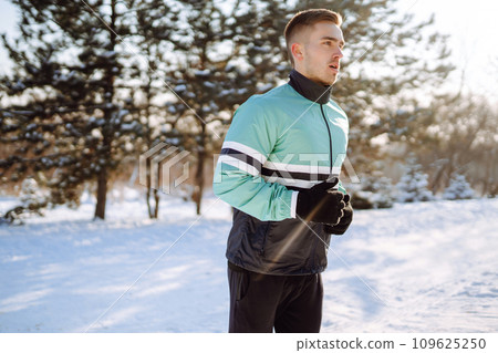 Young sportsman doing workout in forest at snowy winter day. Outdoor fitness, cardio exercises. Young sportsman doing workout in forest at snowy winter day. Outdoor fitness, cardio exercises. 109625250