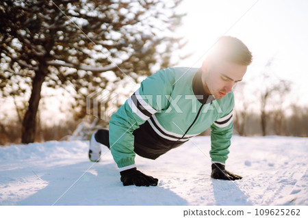 Young sportsman doing workout in forest at snowy winter day. Outdoor fitness, cardio exercises. 109625262