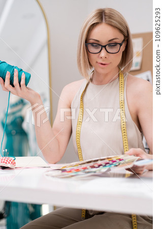 Woman designer chooses color with swatch fan at desk in dressmaking atelier young tailor seeks right material shade for outfit making in sewing workshop Woman designer chooses color with swatch fan at desk in dressmaking atelier young tailor seeks right material shade for outfit making in sewing workshop 109625293