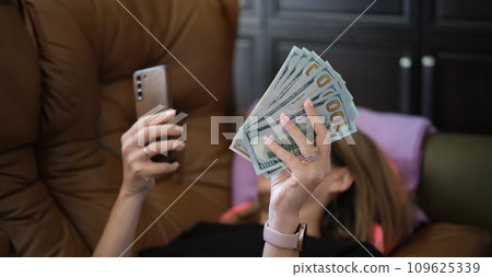 Woman holds smartphone and holds it with dollars Woman holds smartphone and holds it with dollars 109625339