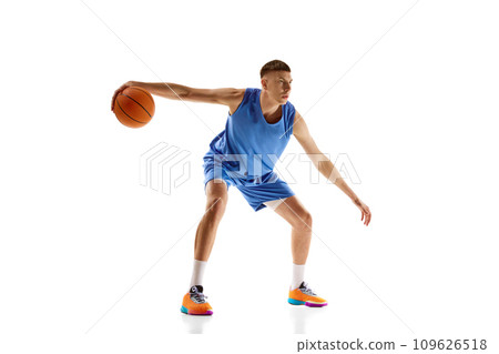 Young man in blue uniform, basketball player in motion during game, dribbling ball isolated over white background. Sport concept 109626518