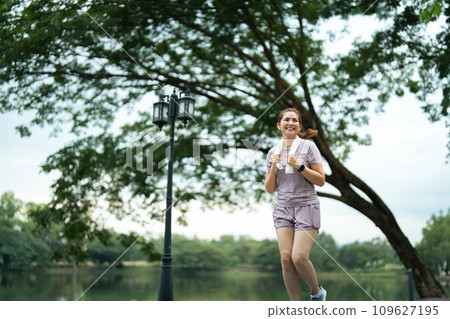 Jogging woman running in park on beautiful day off. Sport fitness model of asian ethnicity training outdoor for marathon Jogging woman running in park on beautiful day off. Sport fitness model of asian ethnicity training outdoor for marathon 109627195