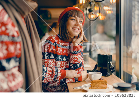 Radiant young woman in a Christmas sweater shares a joyful moment at a cafe Radiant young woman in a Christmas sweater shares a joyful moment at a cafe 109628825