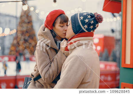 A romantic scene unfolds with a couple kissing gently amidst the twinkling lights of a holiday market, their winter attire adding warmth to the moment 109628845