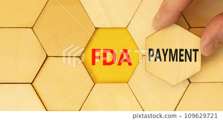 FDA Food and Drug Administration payment symbol. Concept words FDA payment on beautiful wooden puzzle. Beautiful yellow table background. Businessman hand. Business FDA payment concept. Copy space. 109629721