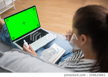 Virtual Doctor Consultation: A sick woman, using nose napkins, has a video call with her doctor while seated on the living room sofa in the comfort of her home.  109629863
