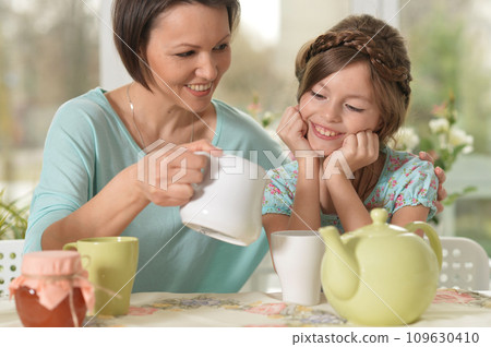 Happy mom and daughter drinking tea at home Happy mom and daughter drinking tea at home 109630410