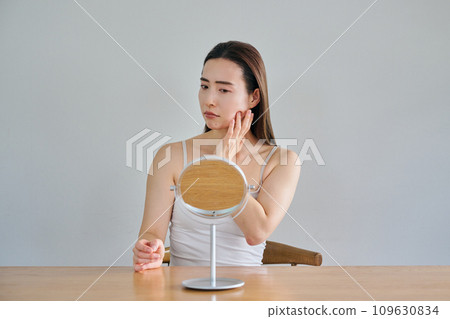 A woman in her 30s worries about wrinkles on her skin while looking in the mirror 109630834