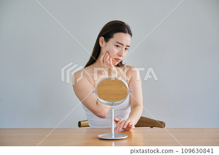 A woman in her 30s worries about wrinkles on her skin while looking in the mirror 109630841