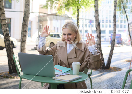 Image of excited blond girl, celebrating, sitting in coffee shop on sunny day, looking at laptop and triumphing 109631077