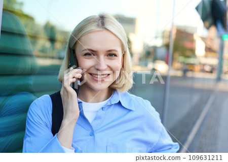 Close up portrait of smiling blond woman, chatting on the phone, talking on mobile telephone, standing on street outdoors 109631211