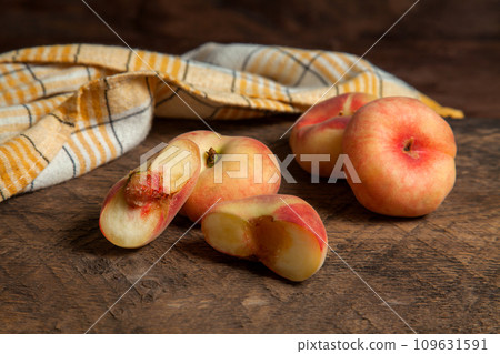 Half and three whole saturn peaches or flat peaches on wooden background with yellow kitchen towel.. Half and three whole saturn peaches or flat peaches on wooden background with yellow kitchen towel.. 109631591