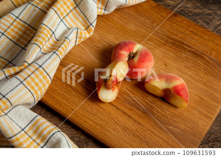 Cutting board with whole and half of saturn peaches or flat peaches on wooden background with yellow kitchen towel.. Cutting board with whole and half of saturn peaches or flat peaches on wooden background with yellow kitchen towel.. 109631593