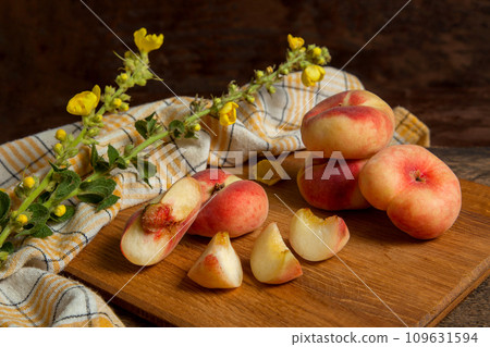 Cutting board with cut and whole saturn peaches or flat peaches on wooden background with yellow kitchen towel.. 109631594