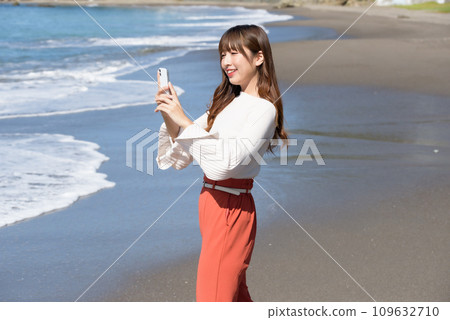 A woman taking pictures of the sea with a smartphone 109632710