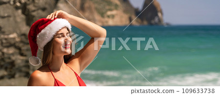 A woman in Santa hat on the seashore, dressed in a red swimsuit. New Year's celebration in a hot country 109633738